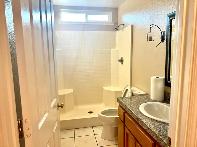 a bathroom with a granite countertop sink a toilet a mirror and shower