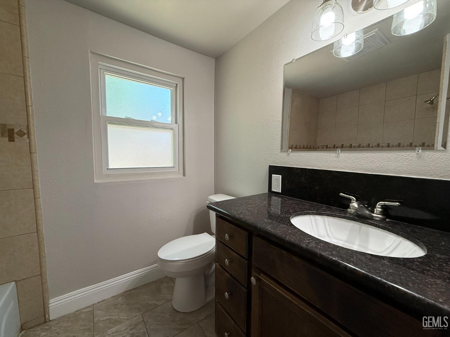 Undisclosed Address Bakersfield, CA 93307 - Photo 10 of 27 a bathroom with a granite countertop sink a toilet and a mirror