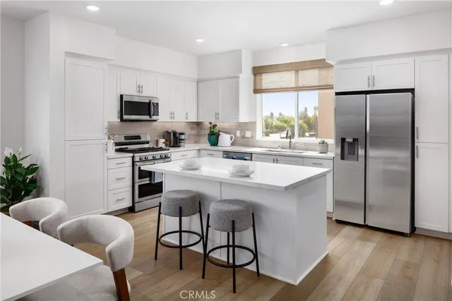 a kitchen with stainless steel appliances a sink a stove a refrigerator cabinets and a dining table with wooden floor