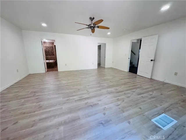 a view of an empty room with wooden floor and a ceiling fan