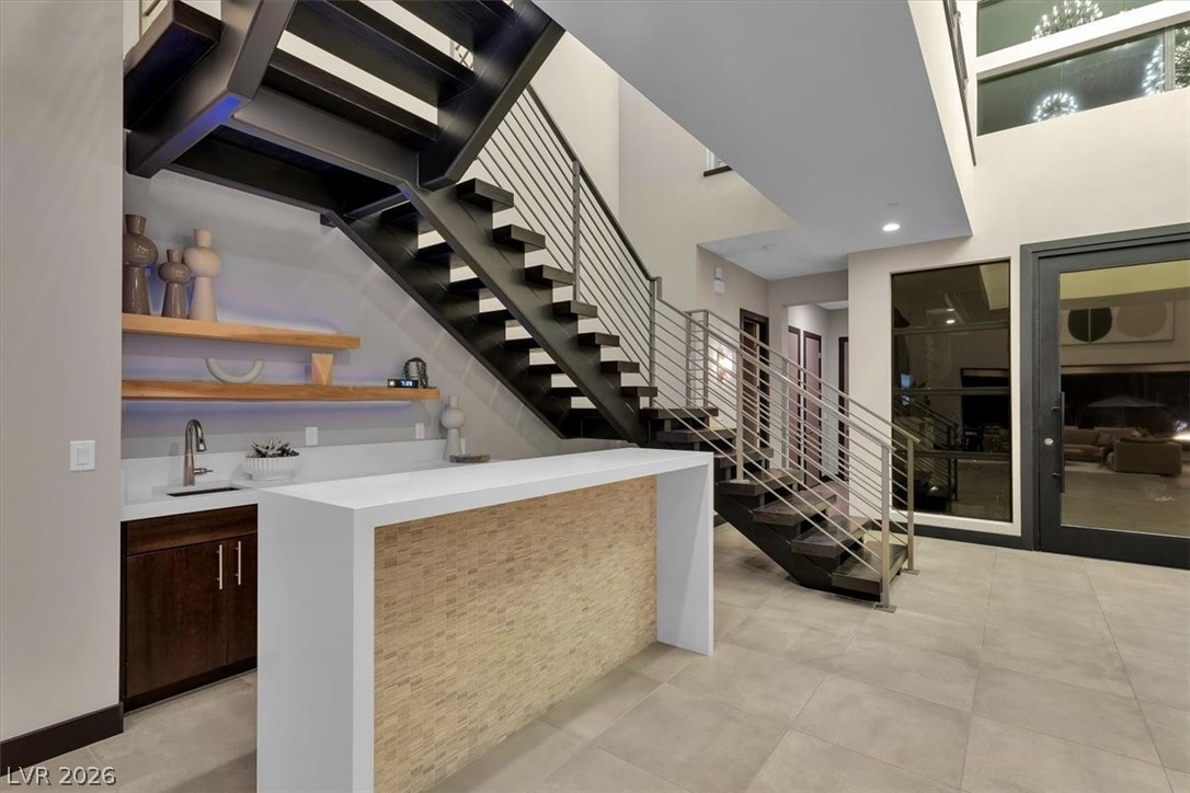 53 Garibaldi Way Henderson, NV 89011 - Photo 13 of 80 Bar featuring modern cabinets, stairs, dark brown cabinetry, light stone counters, and light tile patterned floors