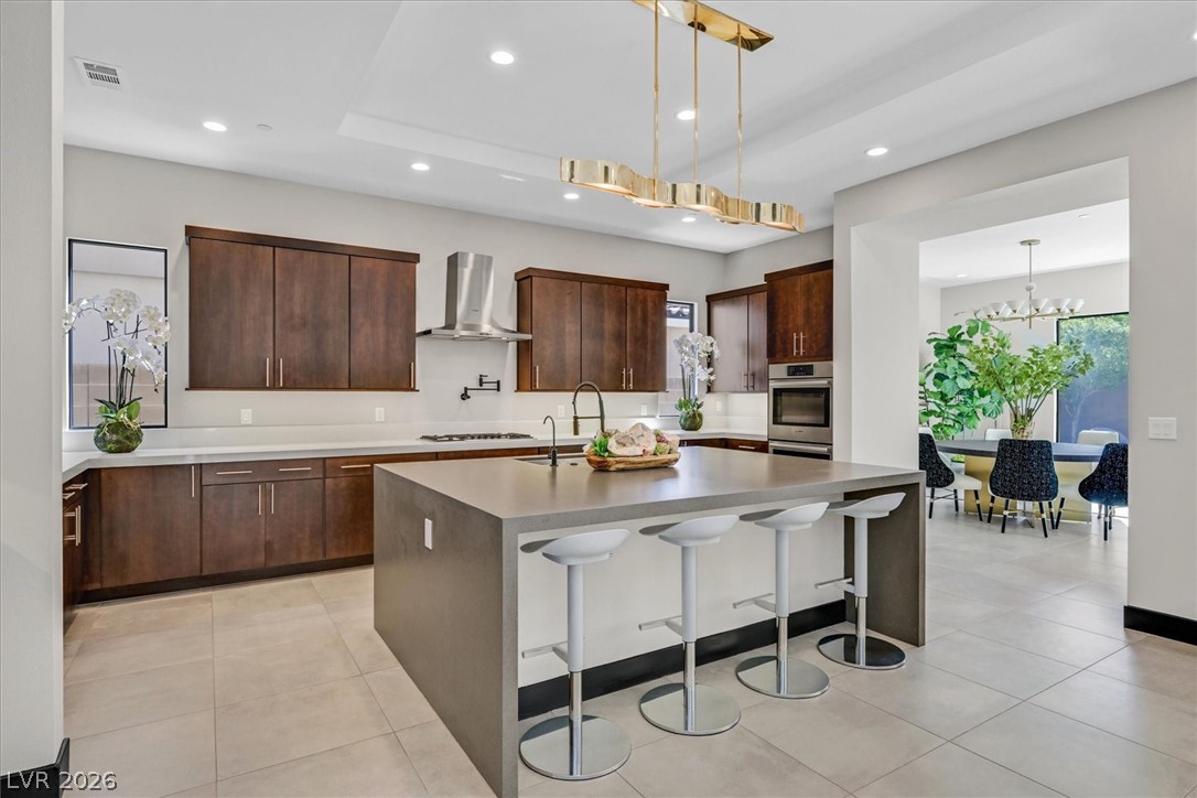53 Garibaldi Way Henderson, NV 89011 - Photo 19 of 80 Kitchen with a kitchen breakfast bar, light stone countertops, an island with sink, a tray ceiling, and pendant lighting