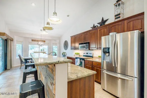 a kitchen with stainless steel appliances granite countertop a refrigerator a stove a sink a dining table and chairs with wooden floor