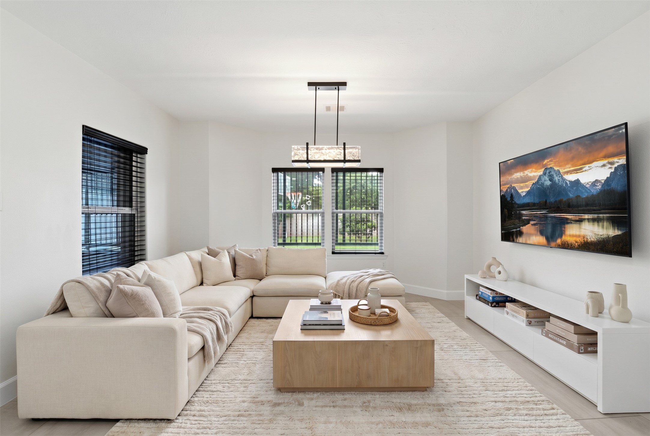 9403 Spaulding Street Houston, TX 77016 - Photo 17 of 50 This photo showcases a modern living room with a cozy beige sectional sofa, a wooden coffee table, and a large wall-mounted TV. The space is bright with natural light from two windows, and features contemporary decor and a neutral color palette.