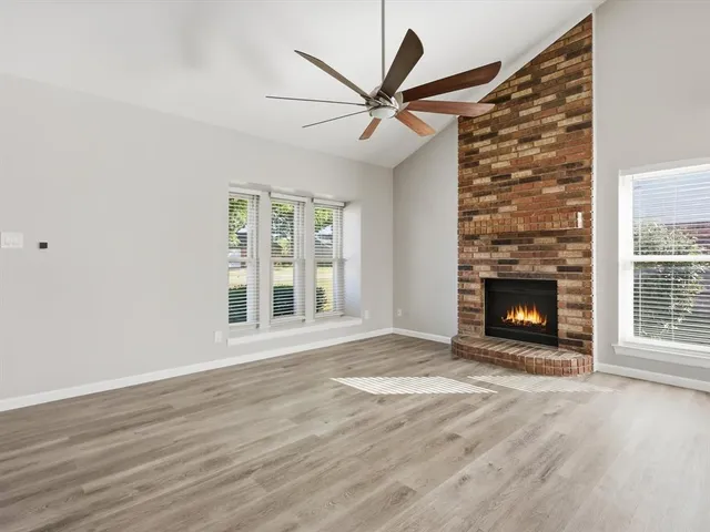 a view of an empty room with wooden floor fireplace and a window