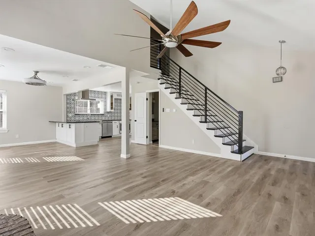a view of an empty room with wooden floor and a ceiling fan