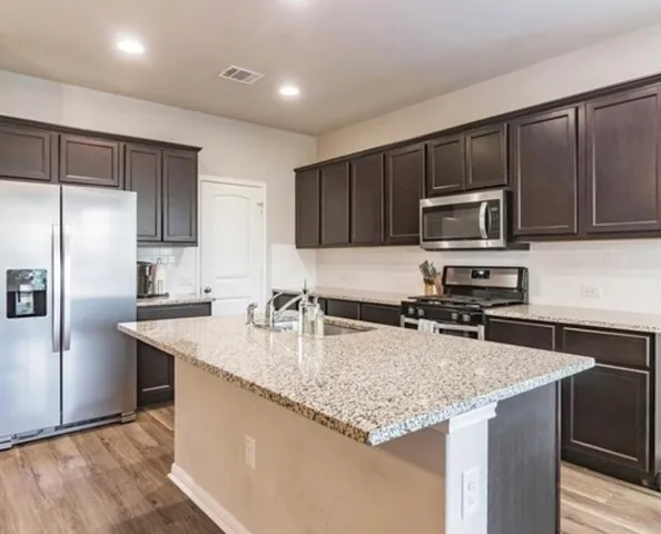 a kitchen with kitchen island granite countertop stainless steel appliances a sink a stove a microwave a refrigerator a sink and cabinets