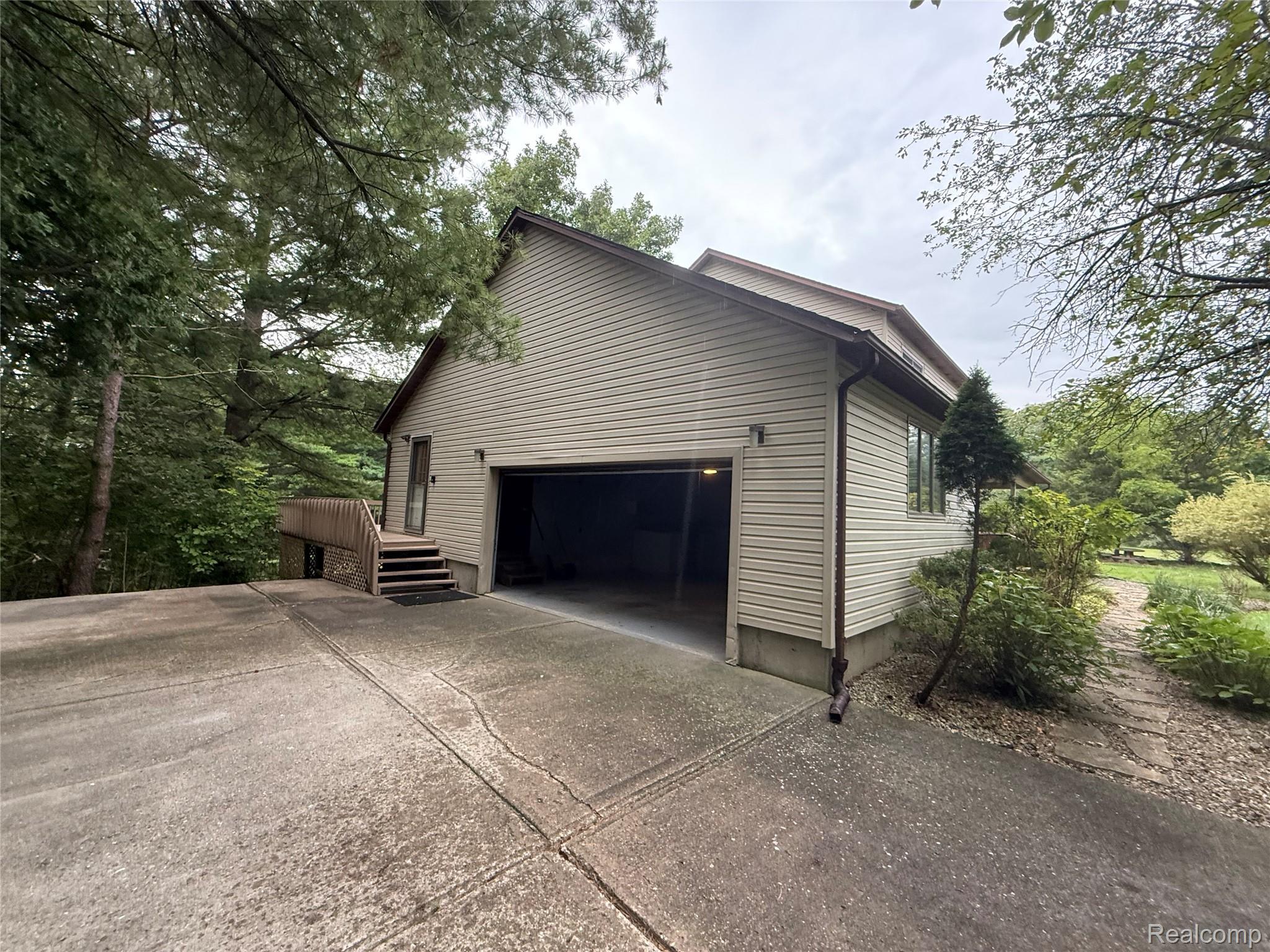 10280 Nimphie Road Fenton, MI 48430 - Photo 3 of 30 Attached two-car garage with a concrete driveway, complemented by a raised wood deck with stairs and surrounding mature trees