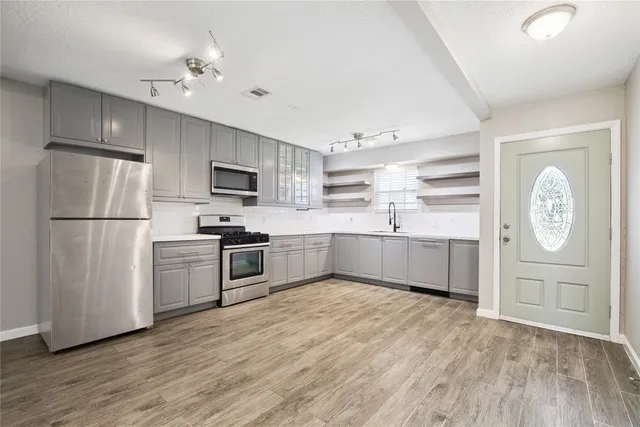 a kitchen with granite countertop a refrigerator oven a sink dishwasher and white cabinets with wooden floor