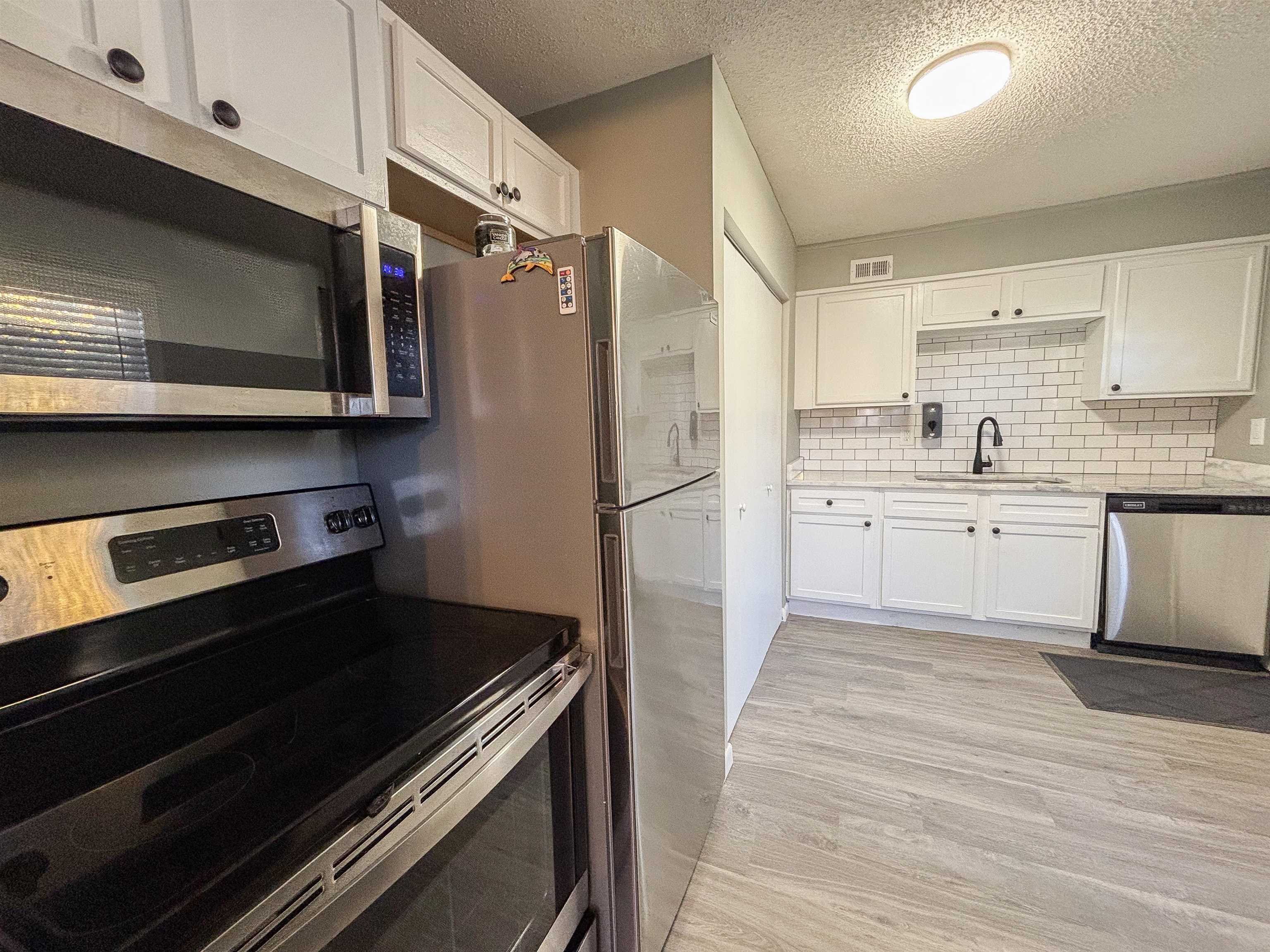 3057 Keats Road Bartlett, TN 38134 - Photo 11 of 23 Kitchen featuring stainless steel appliances, white cabinets, a textured ceiling, light wood-style flooring, and tasteful backsplash
