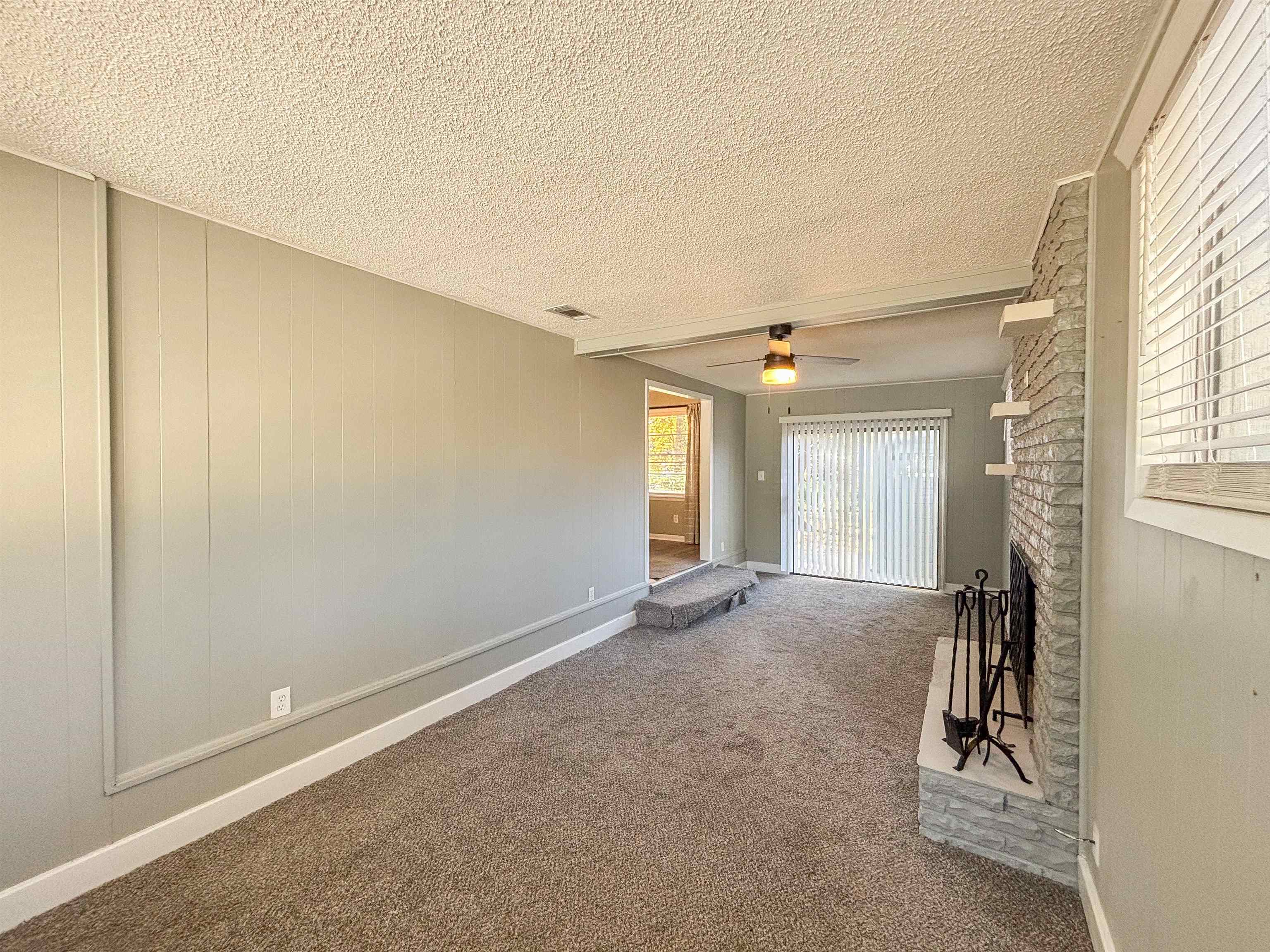 3057 Keats Road Bartlett, TN 38134 - Photo 9 of 23 Unfurnished living room with carpet, a fireplace, a ceiling fan, a textured ceiling, and wood walls
