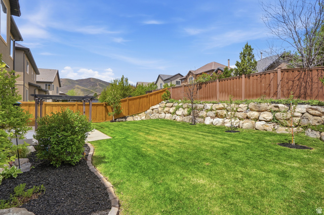 2007 Fielding Hill Lane Draper, UT 84020 - Photo 48 of 83 Expansive backyard featuring a lush lawn, a tiered retaining wall with natural stone, a full privacy fence, a concrete patio, and a dark wood-finish pergola