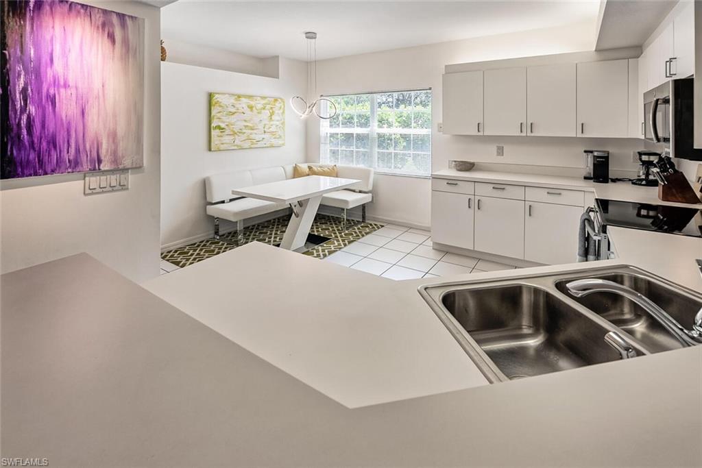 6910 Satinleaf Road North, Unit 101 Naples, FL 34109 - Photo 9 of 30 Kitchen featuring range, sink, white cabinets, hanging light fixtures, and light tile patterned floors