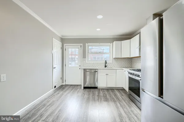 a kitchen with a hard wood floor white cabinets and stainless steel appliances