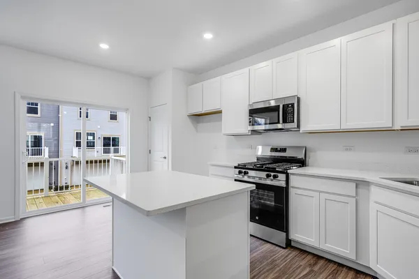 a kitchen with stainless steel appliances granite countertop a stove top oven a sink a refrigerator white cabinets and wooden floor