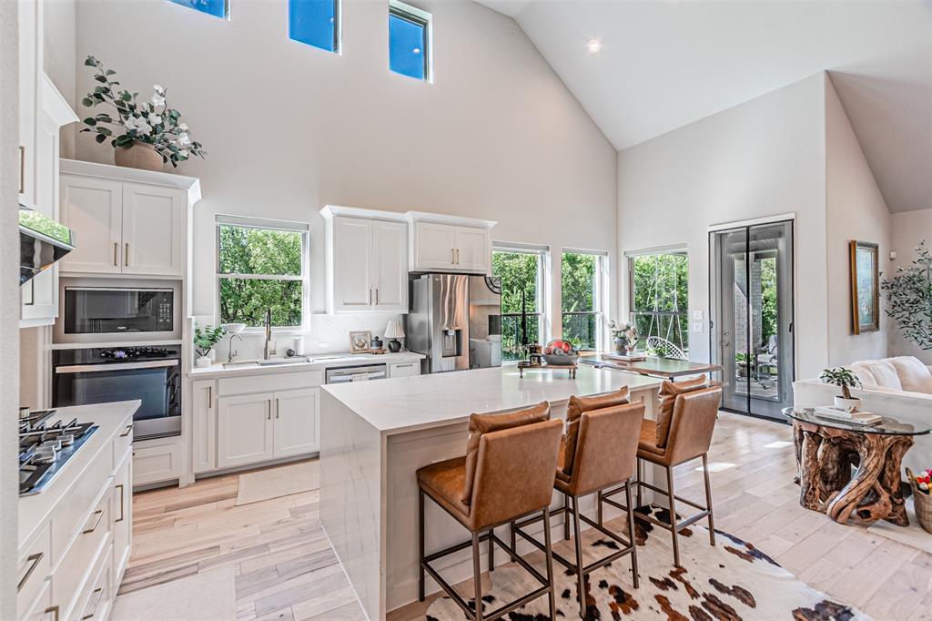 1070 Adair Road Prosper, TX 75078 - Photo 5 of 40 Vaulted ceilings featuring upper transom windows and a contemporary kitchen with white shaker cabinetry, stainless steel appliances, a center island with countertop seating, and light wood-finish flooring