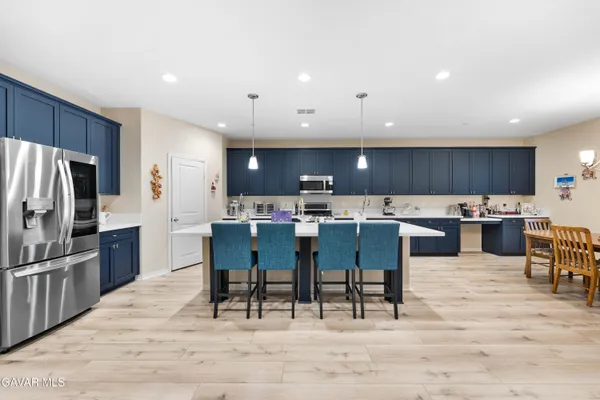 a kitchen with stainless steel appliances kitchen island granite countertop a table chairs sink refrigerator and cabinets