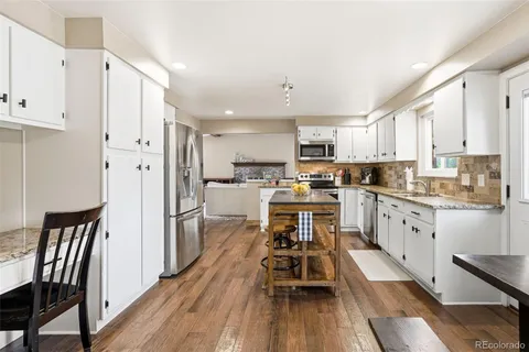 a kitchen with stainless steel appliances a refrigerator a stove top oven a sink dishwasher and white cabinets with wooden floor