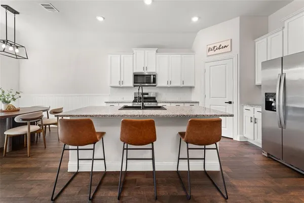 a kitchen with stainless steel appliances granite countertop a dining table chairs and a refrigerator