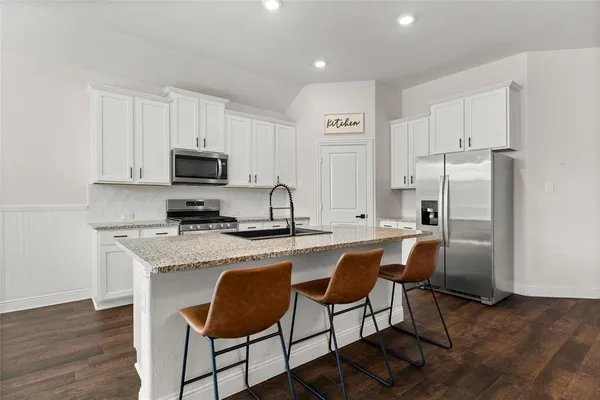 a kitchen with stainless steel appliances granite countertop a stove a sink a microwave a refrigerator and white cabinets with wooden floor