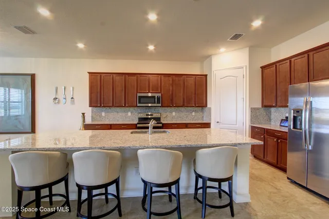 a large kitchen with granite countertop a dining table chairs wooden cabinets and stainless steel appliances
