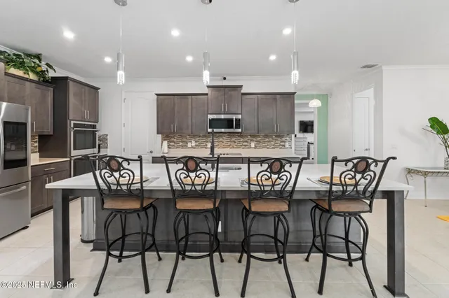 a kitchen with stainless steel appliances kitchen island granite countertop a dining table chairs and a refrigerator