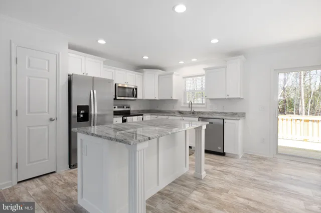 a kitchen with stainless steel appliances granite countertop a stove a sink a refrigerator and white cabinets with wooden floor