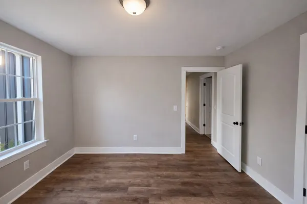 a view of an empty room with wooden floor and a window