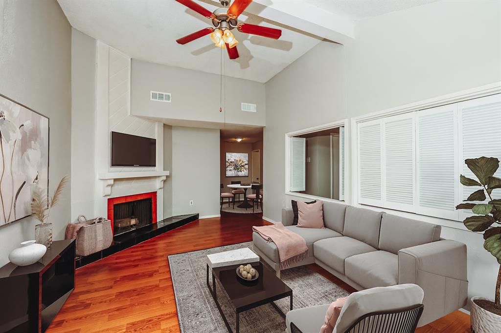 9696 Walnut Street, Unit 1216 Dallas, TX 75243 - Photo 3 of 19 Vaulted ceiling living area featuring hardwood flooring, a fireplace with a black hearth, and white shuttered windows