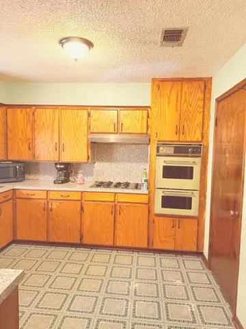 a view of a kitchen with kitchen island granite countertop a sink cabinets and a stove top oven