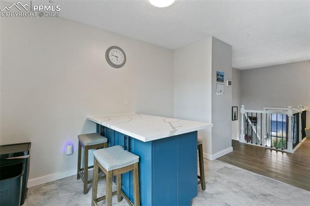 4710 Cheerful Road Colorado Springs, CO 80917 - Photo 15 of 28 Kitchen featuring blue cabinets, a kitchen breakfast bar, a peninsula, light stone counters, and a textured ceiling