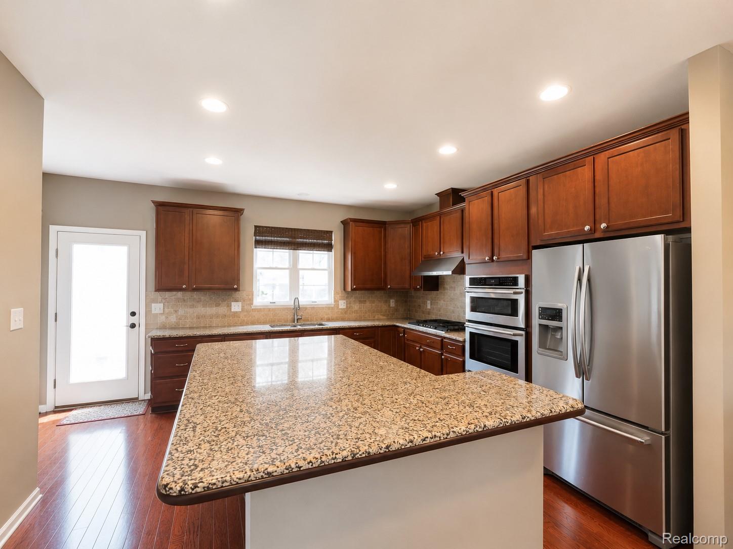 915 Barclay Circle Rochester, MI 48307 - Photo 5 of 14 Kitchen featuring a large island with a speckled countertop, rich wood cabinetry, stainless steel appliances, wood-finish flooring, and recessed lighting