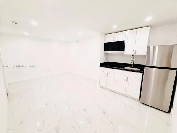 a kitchen with granite countertop a sink a refrigerator a microwave a stove and white cabinets