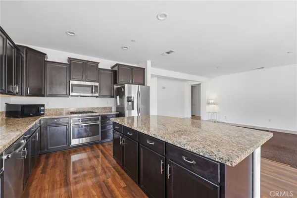 a large kitchen with granite countertop a stove top oven a sink dishwasher and a refrigerator with wooden floor