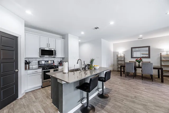 a kitchen with stainless steel appliances kitchen island granite countertop a stove top oven a sink dishwasher a dining table and chairs with wooden floor