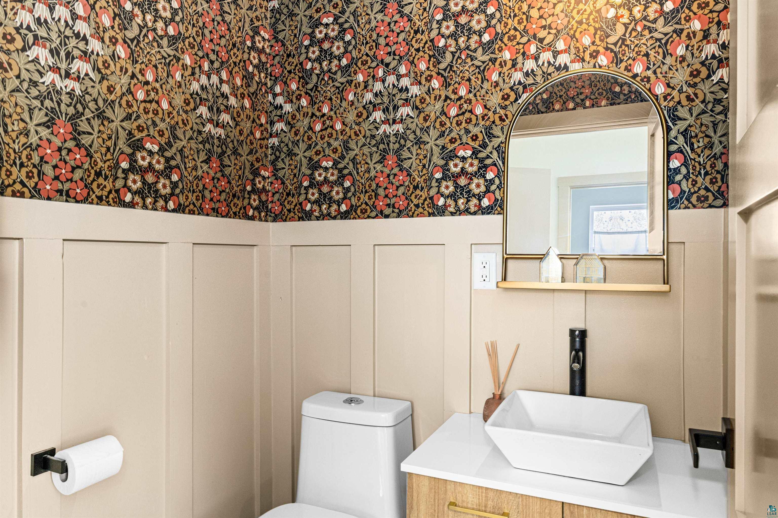 1825 East Shilhon Road Duluth, MN 55804 - Photo 20 of 37 Powder room featuring a decorative floral wallpaper, board and batten wainscoting, an arched mirror with an integrated shelf, a square vessel sink, and a wood-finish vanity with gold hardware