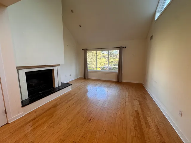 an empty room with wooden floor a fireplace and windows