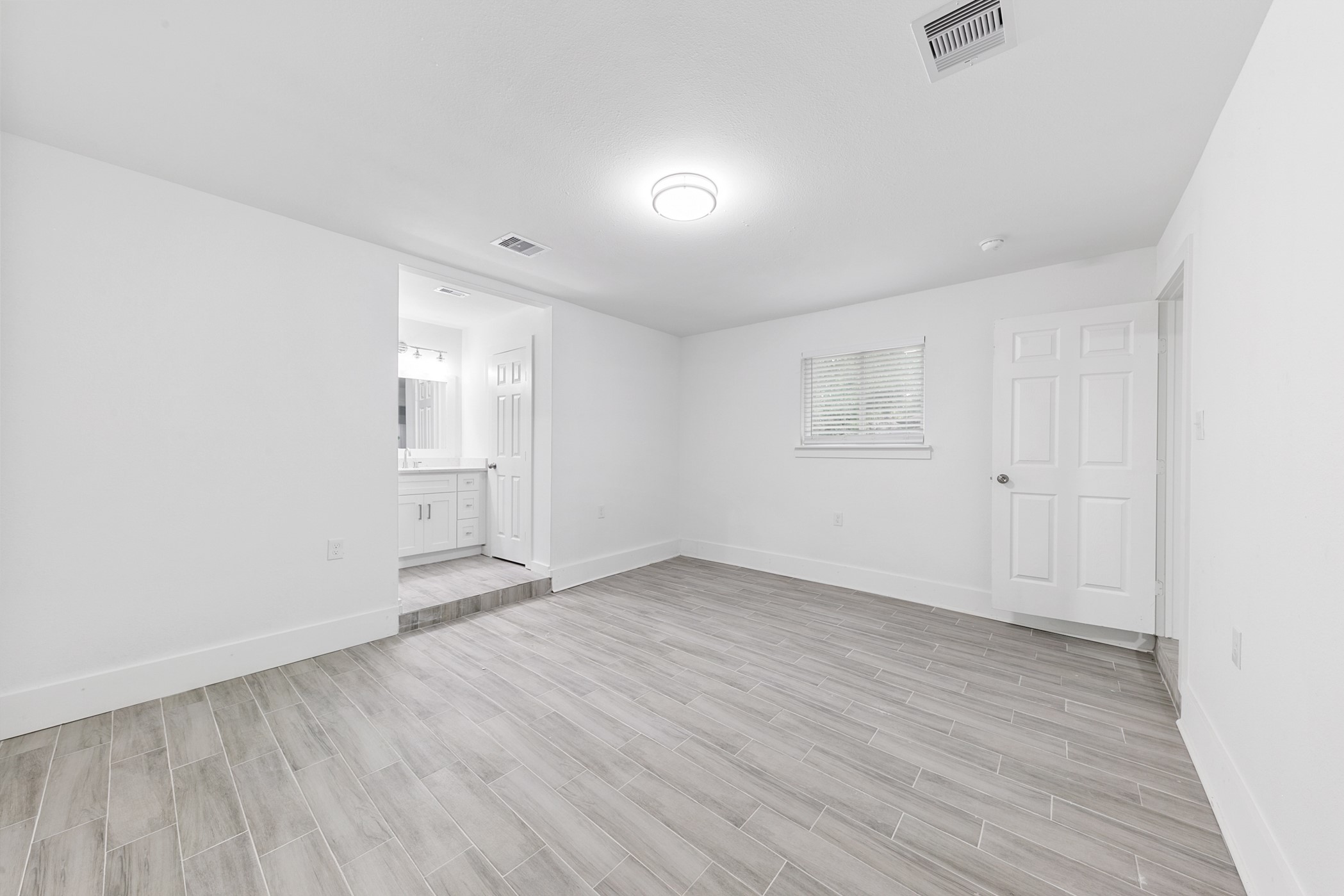6811 McCullum Road Houston, TX 77489 - Photo 11 of 22 Bright and spacious room with light wood-like tile flooring, white walls, and a modern ceiling light. It features a small window and an open entryway leading to a bathroom with white cabinetry.