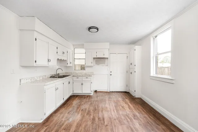 a kitchen with granite countertop a stove a sink and white cabinets with wooden floor