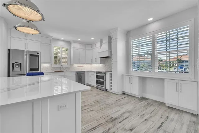 a kitchen with stainless steel appliances granite countertop a sink a stove a refrigerator and white cabinets with wooden floor