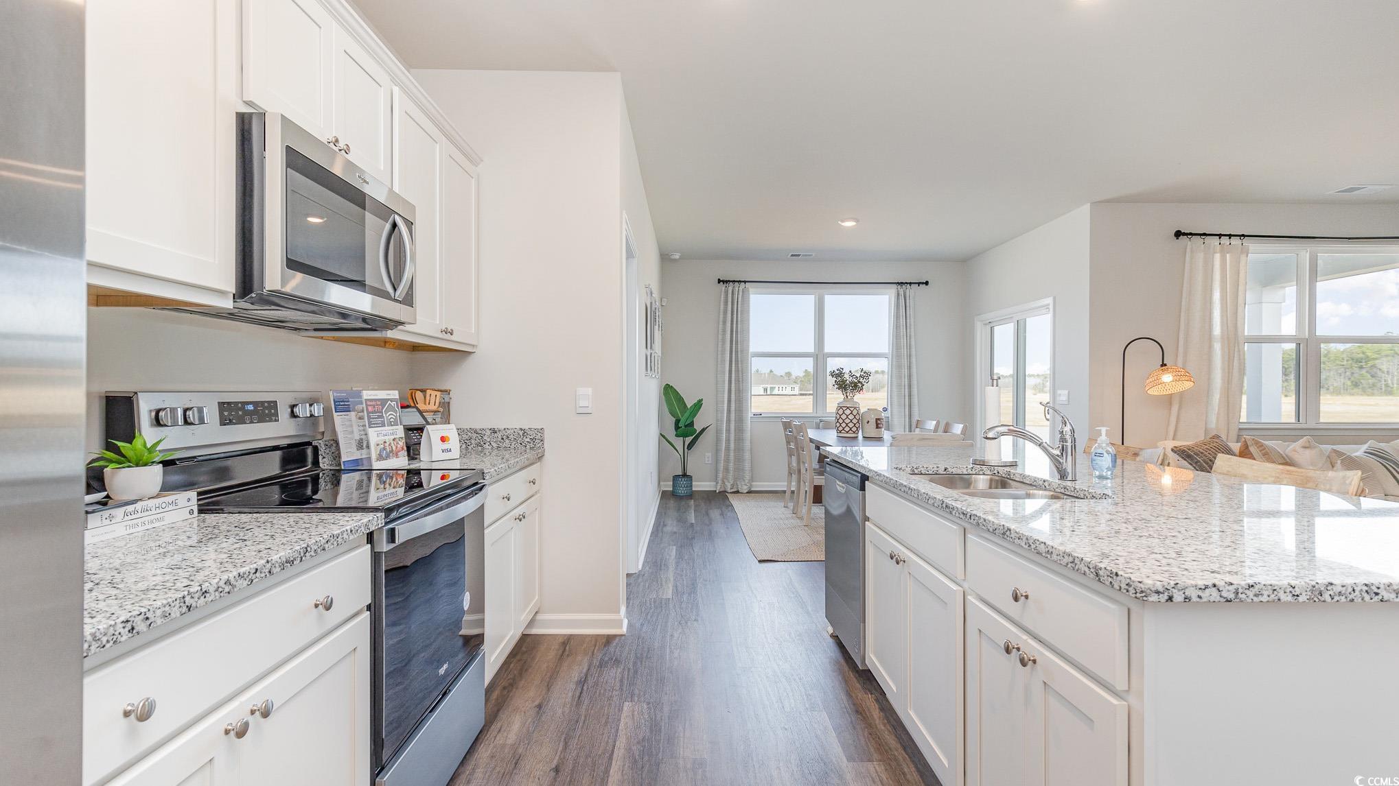 592 Duvall Street Longs, SC 29568 - Photo 5 of 28 Kitchen with appliances with stainless steel finishes, white cabinets, dark wood-type flooring, light stone counters, and a center island with sink
