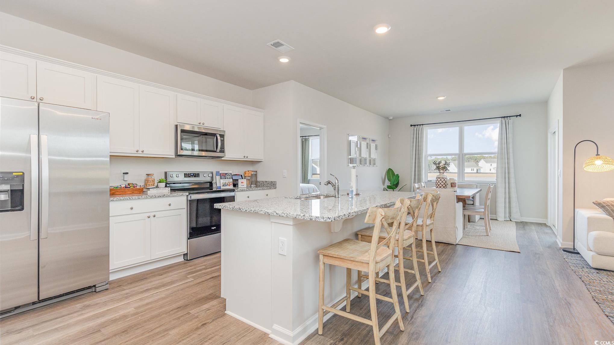 592 Duvall Street Longs, SC 29568 - Photo 6 of 28 Kitchen with appliances with stainless steel finishes, light wood-style flooring, light stone counters, a kitchen breakfast bar, and recessed lighting