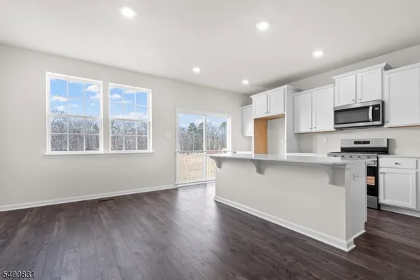 a kitchen with stainless steel appliances granite countertop a stove a sink a refrigerator white cabinets and a large window