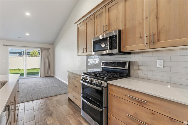2028 West Grace Way Layton, UT 84041 - Photo 11 of 36 Kitchen featuring stainless steel appliances, lofted ceiling, light stone counters, backsplash, and wood finish floors