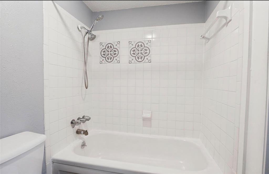 5808 Harvest Hill Road Dallas, TX 75230 - Photo 11 of 18 Bathtub and shower combination featuring white subway tile surround with decorative accent tiles