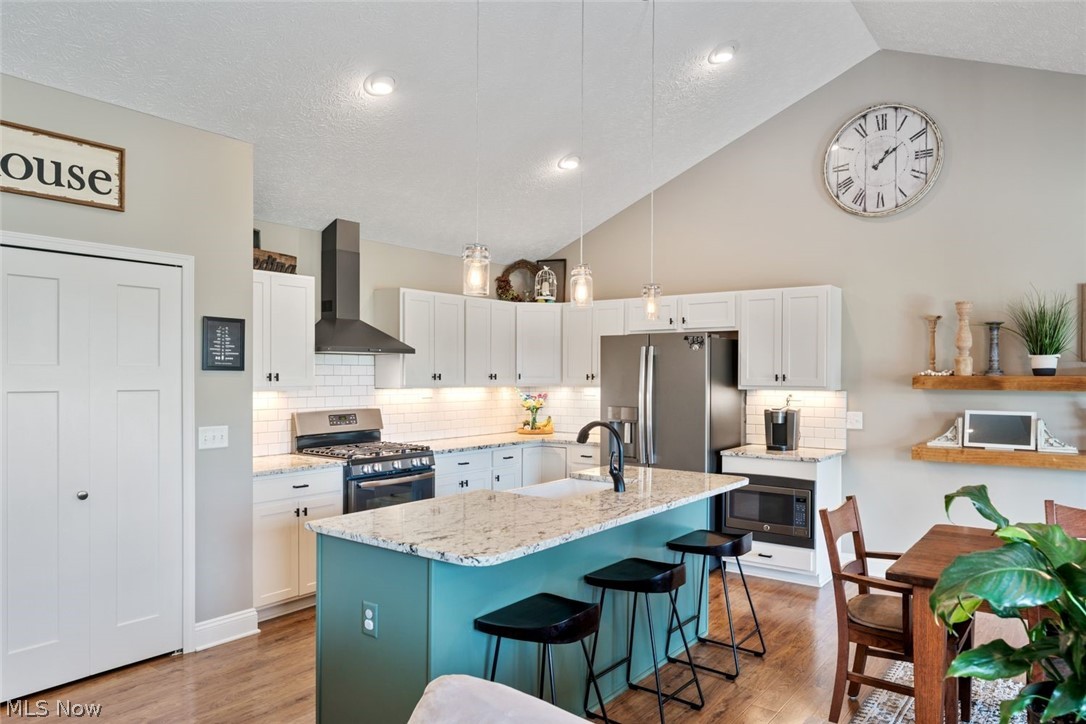 6517 Stone Road Medina, OH 44256 - Photo 14 of 47 Kitchen featuring vaulted ceiling, light hardwood / wood-style flooring, stainless steel appliances, and wall chimney exhaust hood