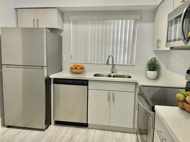 a kitchen with stainless steel appliances a refrigerator a sink a stove and white cabinets