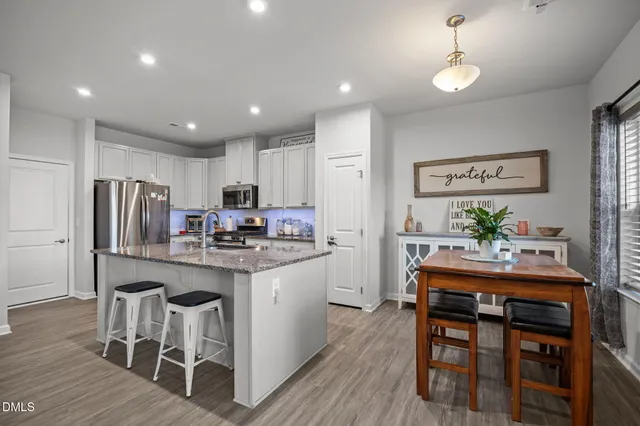 a kitchen with stainless steel appliances granite countertop a dining table chairs stove refrigerator and cabinets