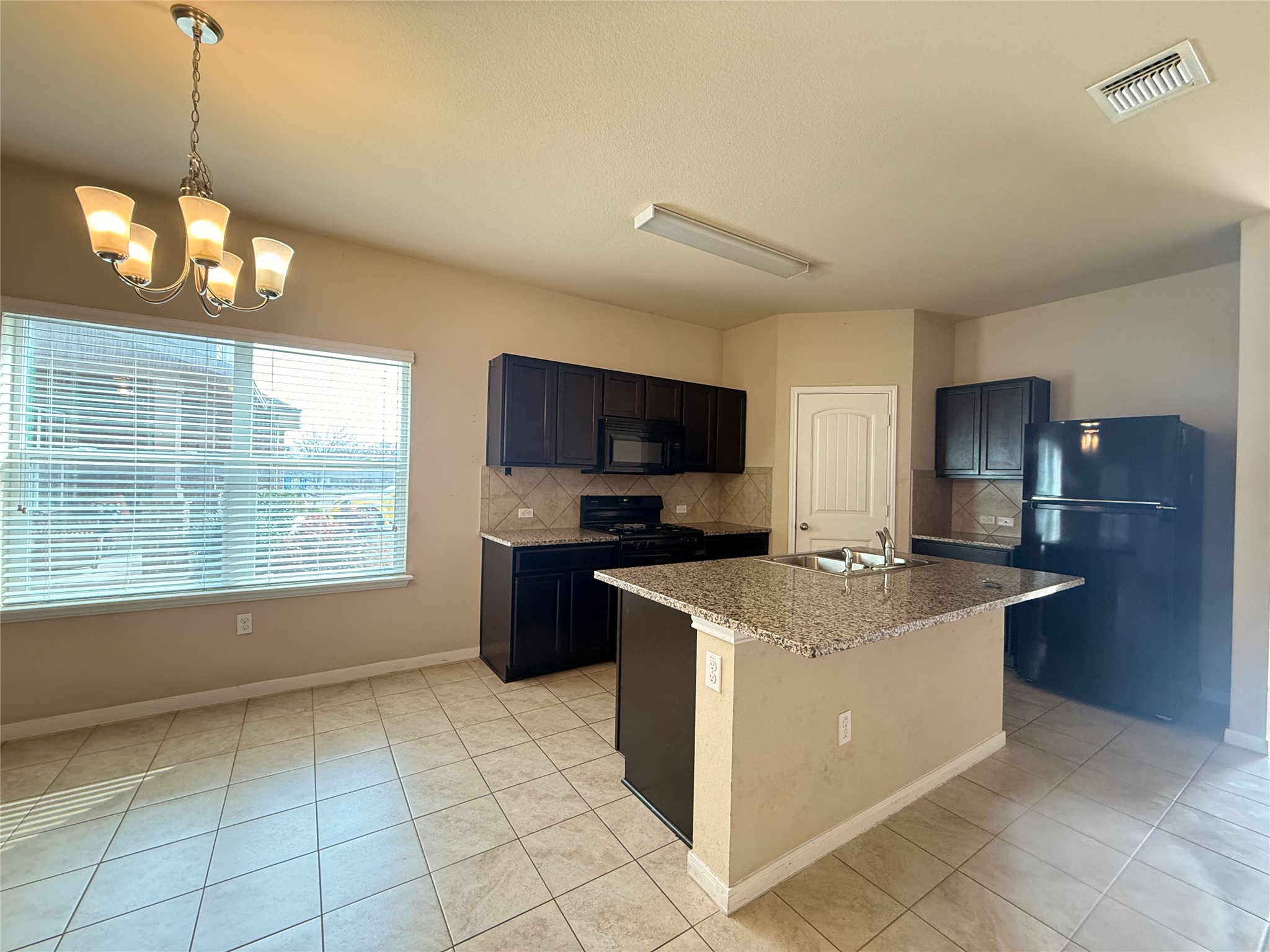 1602 Atlantica Street Cedar Park, TX 78613 - Photo 6 of 24 Kitchen featuring black appliances, decorative backsplash, light stone counters, a center island with sink, and a chandelier