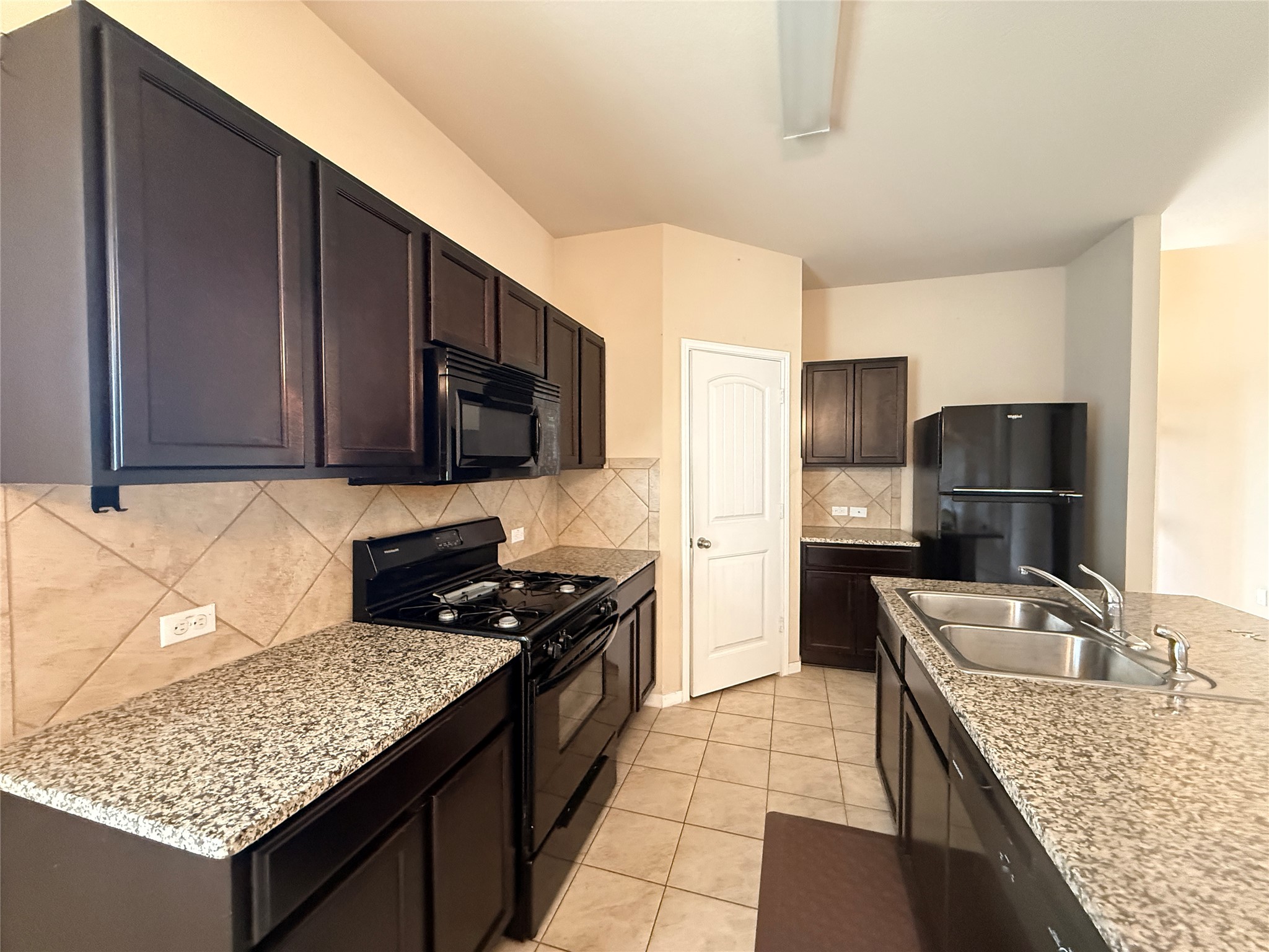 1602 Atlantica Street Cedar Park, TX 78613 - Photo 7 of 24 Kitchen with black appliances, dark wood finish cabinetry, light tile patterned floors, and backsplash